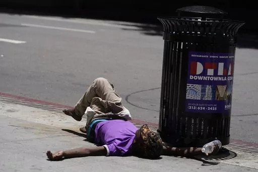 A homeless person lies on the sidewalk while holding a water bottle, Sunday, July 2, 2023, in downtown Los Angeles. Excessive heat warnings remain in place in many areas across the U.S. and are expected to last at least through Monday. (AP Photo/Damian Dovarganes)