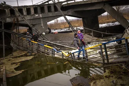 Local militiaman Valery, 37, carries a child as he helps a fleeing family across a bridge destroyed by artillery, on the outskirts of Kyiv, Ukraine, Wednesday, March 2. 2022.  Russian forces have escalated their attacks on crowded cities in what Ukraine's leader called a blatant campaign of terror. (AP Photo/Emilio Morenatti)