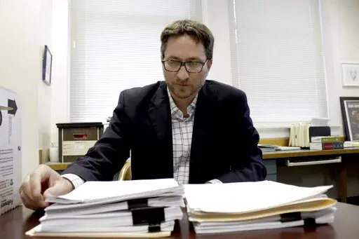 Carl Macpherson, executive director at Metropolitan Public Defender, examines the file in a double murder case that was recently pushed back for trial in his office in Portland, Ore., on May 5, 2022. Macpherson says his firm of 90 public defenders recently stopped taking certain types of new criminal cases for a month in two local courts because they had so many cases that the attorneys were violating their ethical obligations to clients. A post-pandemic glut of delayed cases has exposed shockin