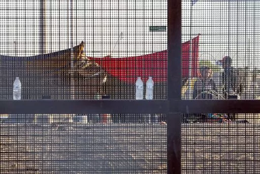 Two migrants, part of a small group, are seeing through the mesh of the border fence as they camp outside a gate in El Paso, Texas, Friday, May 12, 2023. Migrant children in makeshift camps along the U.S.-Mexico border who are waiting to be processed by Border Patrol are in the agency's custody _ something the agency had denied _ and said the Department of Homeland Security must quickly process them and place them in facilities that are “safe and sanitary.”(AP Photo/Andres Leighton, File)