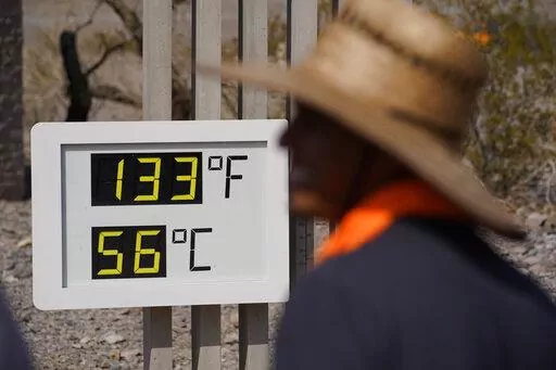 People visit a thermometer on July 11, 2021, in Death Valley National Park, Calif. A special United Nations panel is putting the finishing touches on a major science report that's supposed to tell people the "so what?" about climate change. The report will highlight how global warming disrupts people's lives, their natural environment and Earth itself. (AP Photo/John Locher, File)