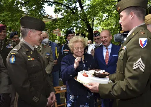 Soldiers from U.S. Army Garrison Italy return a birthday cake to Meri Mion, center, in Vicenza, northern Italy, Thursday, April 28, 2022, to replace the one U.S. soldiers ate as they entered her hometown during one of the final battles of World War II. Meri Mion, who turns 90 on Friday, wiped away tears as she was presented with the cake. Mion was a 13-year-old when Americans came to her nearby village, San Pietro in Gù. (Laura Krieder, U.S. Army via AP)
