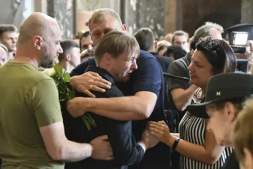 Friends hug Yaroslav Bazylevych during the funeral service for his family in the Garrison Church in Lviv, Ukraine, Friday, Sept. 6, 2024. Bazylevych's wife Yevgenia and their three daughters - Darina, 18, Emilia, 7, and Yaryna, 21 - were killed in Wednesday's Russian missile attack. (AP Photo/Mykola Tys)