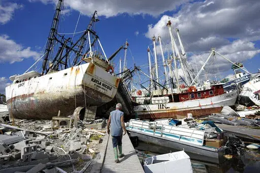 Bruce Hickey, 70, walks along the waterfront littered with debris, including shrimp boats, in the mobile home park where he and his wife Kathy have a winter home, a trailer originally purchased by Kathy's mother in 1979, on San Carlos Island, Fort Myers Beach, Fla., Wednesday, Oct. 5, 2022, one week after the passage of Hurricane Ian. (AP Photo/Rebecca Blackwell)