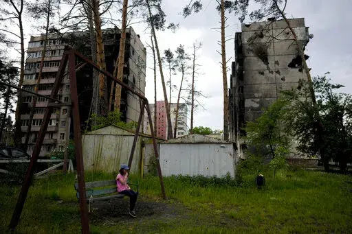 A girl sits on a swing outside destroyed buildings during attacks in Irpin outskirts Kyiv, Ukraine, Monday, May 30, 2022. (AP Photo/Natacha Pisarenko)
