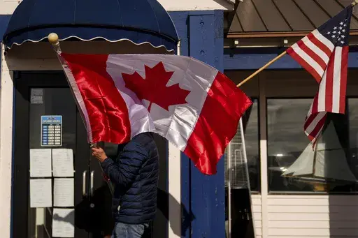 A worker at The Pier, one of three restaurants in town, readjusts Canadian and American flags hanging outside the business, Monday, March 17, 2025, in Point Roberts, Wash. (AP Photo/Lindsey Wasson)