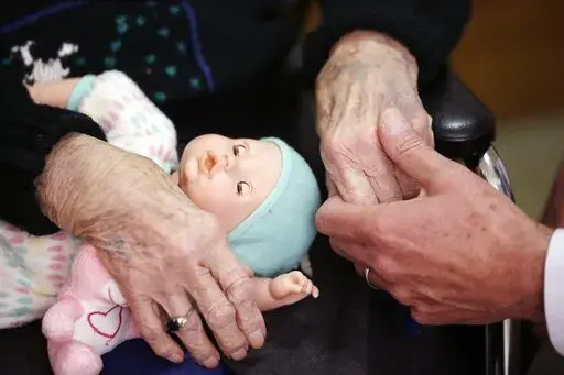 In this April 14, 2016, file photo, a son, at right, holds his mother's hand as they talk at her nursing home in Adrian, Mich.  When parents die, their adult children often must manage their financial affairs. Those kids and other caregivers are left in an unfortunate position if families don’t plan for this reality. On top of managing grief, adult children must guess at their parents’ wishes. And they may have to spend their own money to pay for their parents’ bills and end-of-life arrang