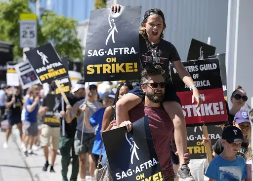 Director of Photography Jac Cheairs and his son, actor Wyatt Cheairs, 11, take part in a rally by striking writers and actors outside Netflix studio in Los Angeles on Friday, July 14, 2023. (AP Photo/Chris Pizzello, File)