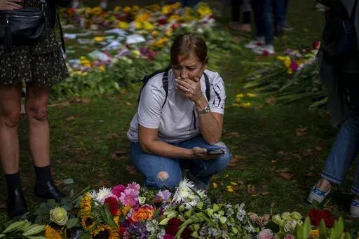 A woman reacts next to flowers and messages for Queen Elizabeth II at the Green Park memorial, near Buckingham Palace, in London, Sept. 10, 2022. Because she reigned and lived for so long, Queen Elizabeth II's death was a reminder that mortality and the march of time are inexorable. (AP Photo/Emilio Morenatti, File)