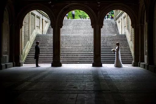 In this Tuesday, May 23, 2017 file photo, a bride and groom pose for wedding pictures at the Bethesda Terrace in New York's Central Park. Industry experts predict 2.5 million weddings in the U.S. this year, a 40-year high. That means millions of invited guests are weighing whether to attend — and how to cover costs if they do.   (AP Photo/Mary Altaffer, file)