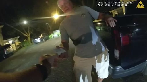 In this image from video provided by the Tampa Police Department, Joseph Ruddy, a prosecutor with the U.S. Attorney’s Office in Tampa, hands his business card to Officer Taylor Grant, outside his home in Temple Terrace, Fla., on the evening of July 4, 2023. When police arrived at his house to investigate a hit-and-run, Ruddy, one of the nation’s most prolific federal narcotics prosecutors, was so drunk he could barely stand up straight, leaning on the tailgate of his pickup to keep his balan