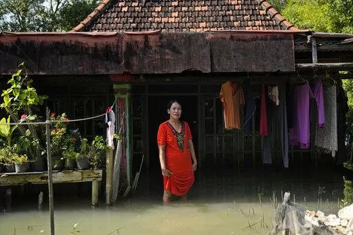 Zuriah stands outside her flooded home in Mondoliko, Central Java, Indonesia, Monday, Aug. 1, 2022. Unable to afford to move to a new home, Zuriah continues to live in the house even as nearly all of her neighbors move away. (AP Photo/Dita Alangkara)
