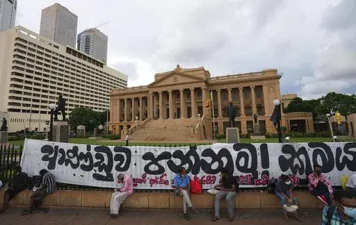 Sri Lankans sit by the fence of the president's office during an on going protest demanding president Gotabaya Rajapaksa resign, in Colombo, Sri Lanka, Friday, April 29, 2022. Gotabaya has agreed to replace his older brother as prime minister in a proposed interim government to solve a political impasse caused by the country's worst economic crisis in decades, a prominent lawmaker said Friday.Banner reads "Oust the government , Change the system." (AP Photo/Eranga Jayawardena)
