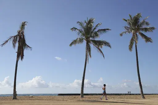 A beachgoer walks down Waikiki Beach, Thursday, Oct. 15, 2020, in Honolulu. About two years after 13 children and teens in Hawaii sued the state over the threat posed by climate change, both sides reached a settlement that includes an ambitious requirement to decarbonize Hawaii’s transportation system in the next 21 years. (AP Photo/Marco Garcia, File)