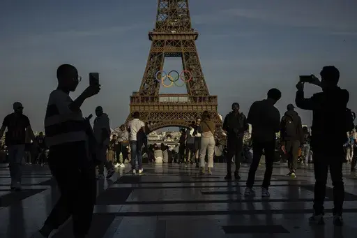 People use their smartphones near the Olympic rings that are displayed on the Eiffel Tower in Paris, June 7, 2024 in Paris. Cybersecurity experts and French officials say Russian disinformation campaigns against France are zeroing in on legislative elections and the Olympic Games which open in Paris at the end of the month. (AP Photo/Aurelien Morissard, File)