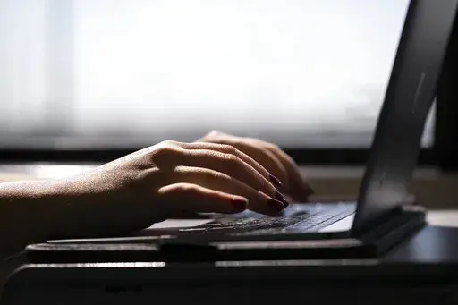 FILE - A woman types on a laptop on a train in New Jersey on May 18, 2021.  When you’re trying to stay accountable and motivated while paying down debt, visual aids can offer encouragement and help you celebrate the small wins. (AP Photo/Jenny Kane)