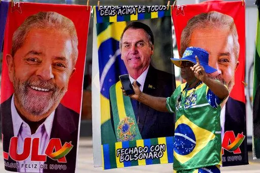 A demonstrator dressed in the colors of the Brazilian flag performs in front of a street vendor's towels for sale featuring Brazilian presidential candidates, current President Jair Bolsonaro, center, and former President Luiz Inacio Lula da Silva, in Brasilia, Brazil, Tuesday, Sept. 27, 2022. Nearly a dozen candidates are running in Brazil’s presidential election but only two stand a chance of reaching a runoff: former President Luiz Inacio Lula da Silva and incumbent Jair Bolsonaro. (AP Phot