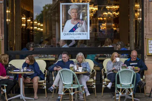 People sit at a terrace bar next to a portrait of Queen Elizabeth II in central London, Tuesday, Sept. 13, 2022. Hotels, restaurants and shops are packed as royal fans pour into the heart of London to experience the flag-lined roads, pomp-filled processions and brave a mileslong line for the once-in-a-lifetime chance to bid adieu to Queen Elizabeth II. (AP Photo/Emilio Morenatti, File)