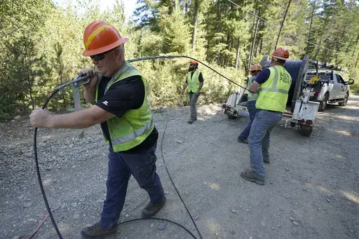 Carl Roath, left, a worker with the Mason County (Wash.) Public Utility District, pulls fiber optic cable on a project to install broadband internet service in the area surrounding Lake Christine near Belfair, Wash., on Aug. 4, 2021. (AP Photo/Ted S. Warren, File)