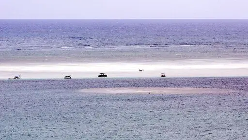 FILE — In this Aug. 15, 2015, file photo, people stand on the sandbar in Hawaii's Kaneohe Bay. Hawaii's Department of Land and Natural Resources is warning people that they face arrest if found burning Christmas trees at an oceanic sandbar. The sandbar found between the open Pacific Ocean and Kaneohe Bay on Oahu's windward side is a popular gathering place for local boaters and tourists. A tradition of piling up Christmas trees for bonfires on the sandbar is harming the environment, officials 