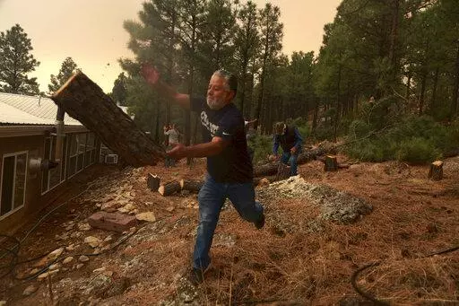 Chris Castillo throws a freshly-cut log as he and his cousins clear a wireline along a family member's home in Las Vegas, N.M., Monday, May 2, 2022. Wind-whipped flames are marching across more of New Mexico's tinder-dry mountainsides, forcing the evacuation of area residents and dozens of patients from the state's psychiatric hospital as firefighters scramble to keep new wildfires from growing. (AP Photo/Cedar Attanasio)
