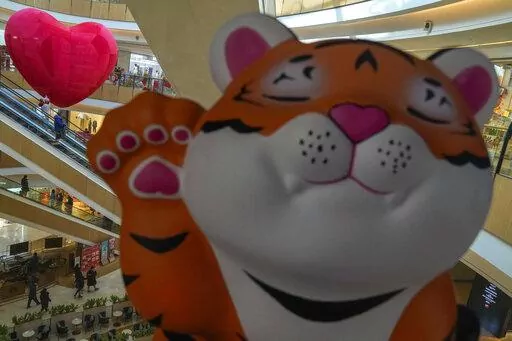 A cartoon tiger is displayed as shoppers wearing face masks to help protect fro the coronavirus ride on escalators at a mall during the Lunar New Year Eve in Beijing, Monday, Jan. 31, 2022. The pandemic is muting Lunar New Year celebrations again this year, though people around Asia are finding ways to mark the traditional holiday despite restrictions on travel, restaurants and large gatherings. The Lunar New Year falls on Tuesday. (AP Photo/Andy Wong)
