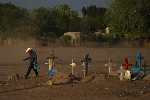 A Yaqui Indigenous wears a bandana over his mouth as he walks through dust past the cemetery where slain water-defense leader Tomás Rojo is buried in Potam, Mexico, Tuesday, Sept. 27, 2022. Rojo was a descendent of Tetabiate, a Yaqui leader killed in a 1901 battle with the government, which deported the surviving Yaquis to work in slave-like conditions on henequen plantations in far-away Yucatan. (AP Photo/Fernando Llano)
