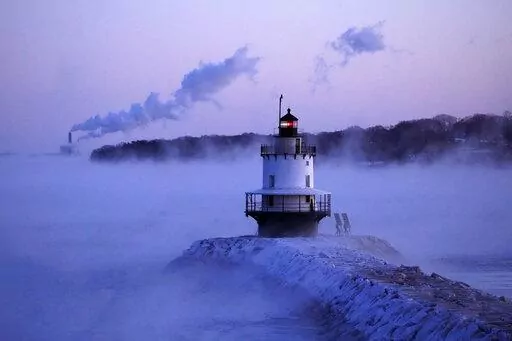 Spring Point Ledge Light is surrounded by arctic sea smoke while emissions from the Wyman Power plant, background, are blown horizontal by the fierce wind, Saturday, Feb. 4, 2023, in South Portland, Maine. The morning temperature was about -10 degrees Fahrenheit. (AP Photo/Robert F. Bukaty)