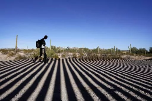 A migrant walks along a road shadowed by the steel columns of the border wall separating Arizona and Mexico after crossing into the United States, Friday, Dec. 15, 2023, near Lukeville, Ariz. (AP Photo/Gregory Bull, File)