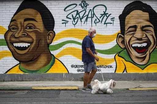 A man walks his dog past a mural of Brazilian soccer stars Pele, left, and Garrincha in Rio de Janerio, Brazil, Friday, Dec. 30, 2022. Edson Arantes do Nascimento, known to the world as Pele, died in Sao Paulo Thursday at the age of 82. (AP Photo/Bruna Prado)