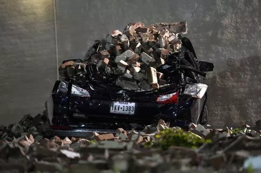 A car crushed by falling bricks from a fallen building wall sits in a downtown parking lot after a severe thunderstorm passed through, Thursday, May 16, 2024, in Houston. (AP Photo/David J. Phillip)