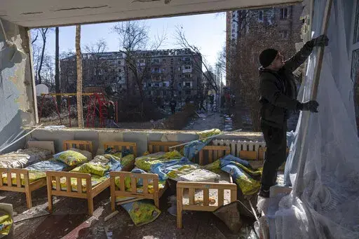 A man removes a destroyed curtain inside a school damaged among other residential buildings in Kyiv, Ukraine, Friday, March 18, 2022. As of early May, the Ukrainian government says Russia has shelled more than 1,000 schools, completely destroying 95. (AP Photo/Rodrigo Abd, File)