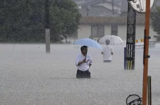 People wade through a street due to a heavy rain in Kurume, Fukuoka prefecture, southern Japan Monday, July 10, 2023. Scientists have long warned that more extreme rainfall is expected in a warming world. (Kyodo News via AP)
