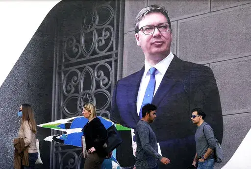 People walk by the pre-election billboard showing Current Serbian President and the Serbian Progressive Party leader Aleksandar Vucic in Belgrade, Serbia, Monday, March 28, 2022. Serbia's populist President Aleksandar Vucic, who has fostered close ties with Russia and refused to impose sanctions against Moscow over its invasion of Ukraine, is expected to extend his almost 10-year grip on power in the Balkan country at an election on Sunday. (AP Photo/Darko Vojinovic)