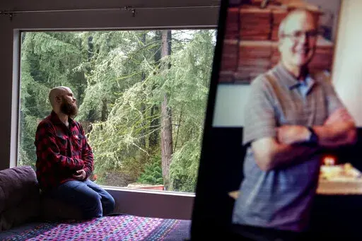 Nathan Lambrecht is photographed next to a picture of his father, Doug Lambrecht, at his apartment in Woodinville, Wash., Monday, March 21, 2022. The 71-year-old retired physician was among the first of the nearly 1 million Americans to die from COVID-19. "I'm afraid that as the numbers get bigger, people are going to care less and less," Nathan said. "I just hope people who didn't know them and didn't have the same sort of loss in their lives due to COVID, I just hope that they don't forget and