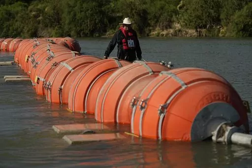 A kayaker walks past large buoys being used as a floating border barrier on the Rio Grande, Aug. 1, 2023, in Eagle Pass, Texas. A federal judge on Wednesday, Sept. 6, ordered Texas to move a large floating barrier to the riverbank of the Rio Grande after protests from the the U.S. and Mexican governments over Republican Gov. Greg Abbott’s latest tactic to stop migrants from crossing America’s southern border. (AP Photo/Eric Gay, File)