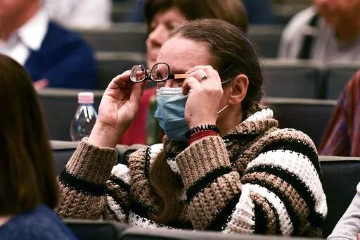 A volunteer ballot counter holds her glasses to see a presentation in Budapest, Hungary, Thursday, March 24, 2022. A grassroots civic initiative in Hungary has recruited more than 20,000 volunteer ballot counters to ensure a fair tally in upcoming elections. In the contest on April 3, Prime Minister Viktor Orban will seek his fourth consecutive term in what polls suggest will be the closest election since he came to power in 2010.(AP Photo/Anna Szilagyi)