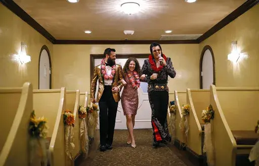 Elvis impersonator Brendan Paul, right, walks down the aisle during a wedding ceremony for Katie Salvatore, center, and Eric Wheeler at the Graceland Wedding Chapel in Las Vegas. Authentic Brands Group (ABG) sent cease-and-desist letters earlier this month to multiple chapels, saying they had to comply by the end of May, the Las Vegas Review-Journal reported. (AP Photo/John Locher, File)