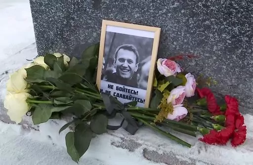 This grab taken from video shows flowers and a portrait of Russian opposition leader Alexei Navalny that Lyudmila Navalnaya, mother of Russian opposition leader Alexei Navalny, put to pay tribute to her son at the at the memorial to victims of political repression, in Salekhard, 1937 km (1211 miles) northeast of Moscow, Russia, on Tuesday, Feb. 20, 2024. Russians across the vast country streamed to ad-hoc memorials with flowers and candles to pay tribute to Alexei Navalny, the most famous Russia