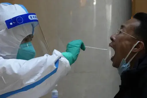 A worker prepares to take swab sample from a man before quarantine for a government event at a hotel on Thursday, April 7, 2022, in Beijing. Amid a surge in COVID cases and growing public frustration, China says it is sticking to its hardline "zero-tolerance" approach mandating lockdowns, mass testing and the compulsory isolation of all suspected cases and close contacts. (AP Photo/Ng Han Guan)