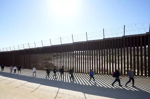 A group of people, including many from China, walk along the wall after crossing the border with Mexico to seek asylum, Tuesday, Oct. 24, 2023, near Jacumba, Calif. As Congress returns this week, Senate Republicans have made it clear they won’t support additional war aid for Ukraine unless they can pair it with border security measures. (AP Photo/Gregory Bull, File)