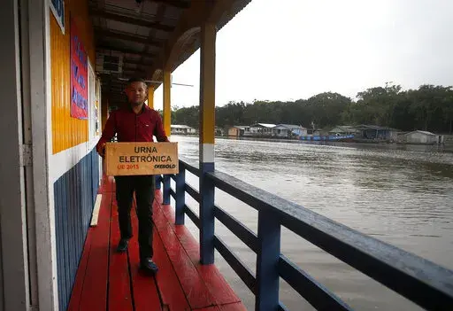 A worker carries an electronic ballot machine at a polling station during general elections in Lago de Catalao, Amazonas state, Brazil, Sunday, Oct. 2, 2022. (AP Photo/Edmar Barros)