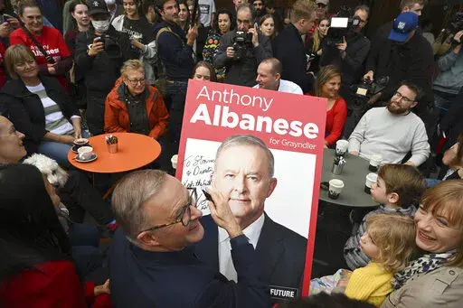 Australia's Prime Minister-elect Anthony Albanese, center, signs a poster for twin brothers Dimitri and Stavros, bottom right, as he visits a coffee shop in suburban Marrickville, Sydney, Sunday, May 22, 2022. Albanese has promised to rehabilitate Australia's international reputation as a climate change laggard with steeper cuts to greenhouse gas emissions. (Dean Lewins/AAP Image via AP)