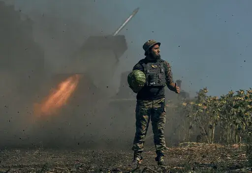 A Ukrainian soldier holds a watermelon and thumbs up as a rocket launch system fires in the font line in Donetsk region, eastern Ukraine, Saturday, Aug. 3, 2022. (AP Photo/Kostiantyn Liberov)