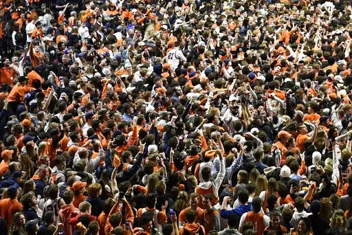Fans storm the court at the conclusion of a college basketball game in Champaign, Ill., on Sunday, March 6, 2022. After about two months of falling COVID-19 cases, pandemic restrictions have been lifted across the U.S., and many people are taking off their masks and returning to indoor spaces. (AP Photo/Michael Allio)