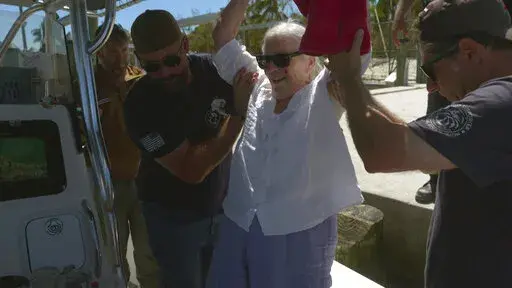 A team from the non-profit Project Dynamo helps Betty Reynolds onto a boat as she is rescued from Sanibel Island, Fla., Saturday, Oct. 1, 2022. Reynolds home was flooded when Hurricane Ian swept through the area. (AP Photo/Robert Bumsted)