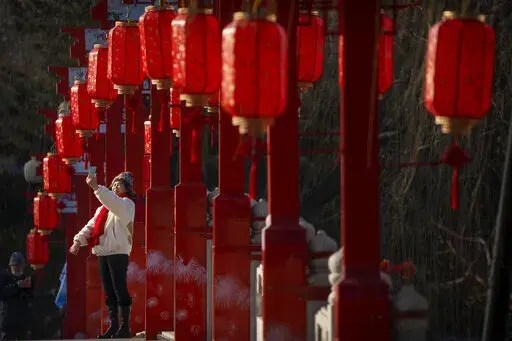 A woman poses for a selfie on a bridge decorated with lanterns at a public park in Beijing on the first day of the Lunar New Year holiday, Sunday, Jan. 22, 2023. (AP Photo/Mark Schiefelbein)