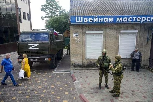 Russian soldiers guard an office for Russian citizenship applications as their military truck is parked nearby, in Melitopol, south Ukraine, on July 14, 2022. As Russians seized parts of eastern and southern Ukraine in the 8-month-old war, mayors, civilian administrators and others, including nuclear power plant workers, say they have been abducted, threatened or beaten to force their cooperation. In some instances, they have been killed. Human rights activists say these actions could constitute