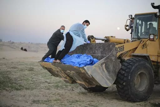 Bulldozer carries the bodies of Palestinians killed in the north of the Gaza Strip and turned over by the Israeli military during a mass funeral in Rafah, Tuesday, Dec. 26, 2023. (AP Photo/Hatem Ali)