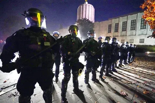 Police line-up at the Oregon State Capitol building where demonstrators gathered during the day Saturday, Nov 7, 2020, in Salem, Ore. A federal civil rights trial against three former Minneapolis police officers seeks to hold them responsible for not stopping George Floyd's murder under Derek Chauvin's knee — and perhaps strike a blow against longstanding police culture that breeds reluctance to rein in fellow officers. (AP Photo/Marcio Jose Sanchez, File)